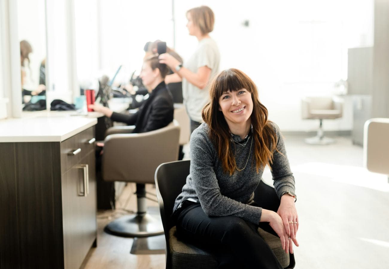 A salon owner sitting in her studio while stylists work with clients behind her