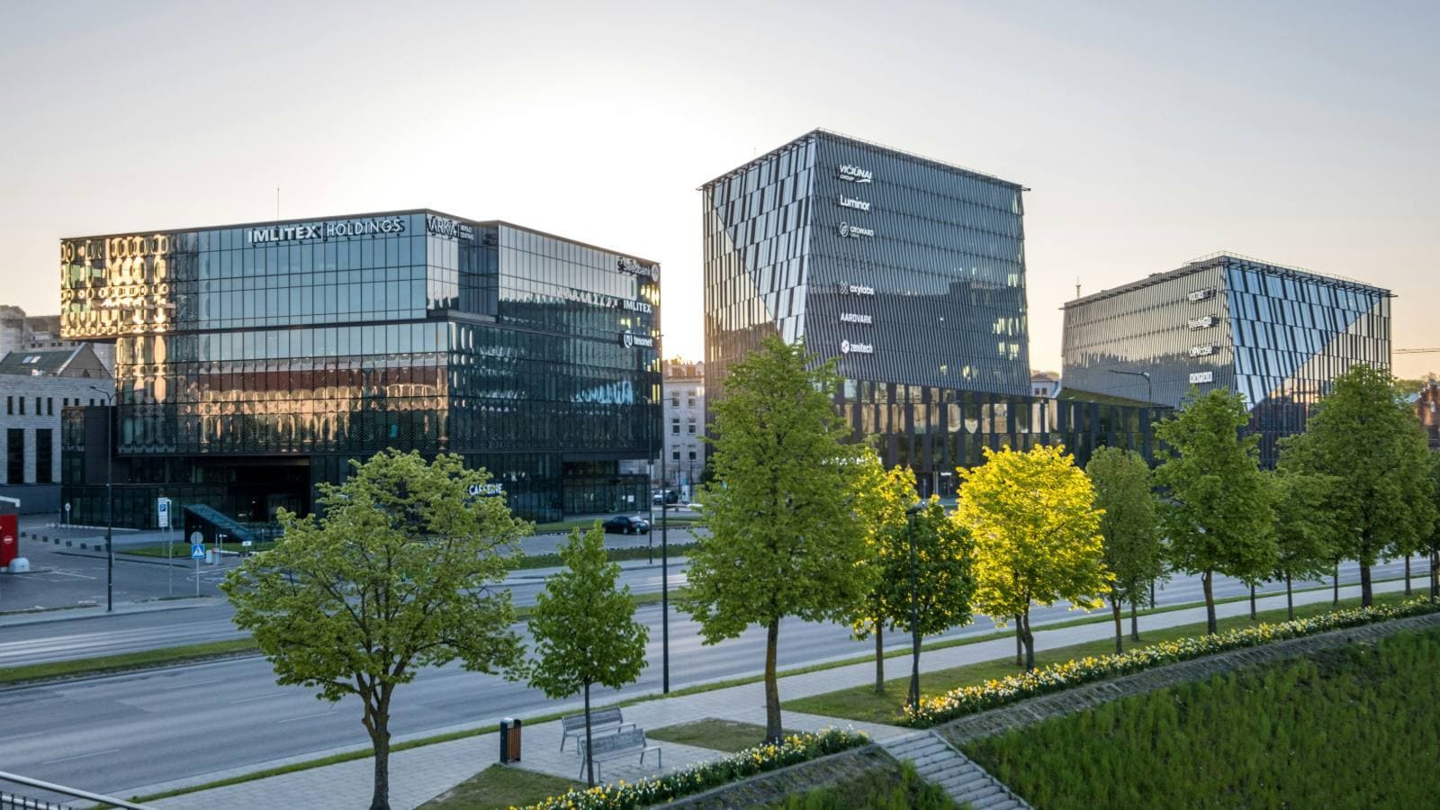 Modern glass commercial office buildings at dusk, seen from a tree-lined boulevard
