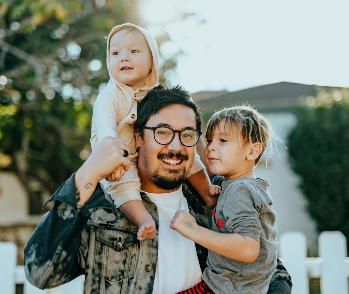 A father carrying his two young children in the front yard of their home