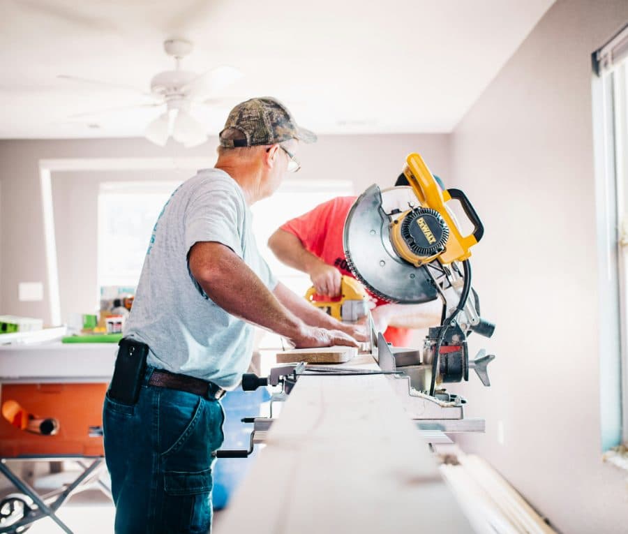 Two tradespeople cutting timber on a drop saw inside a house under construction