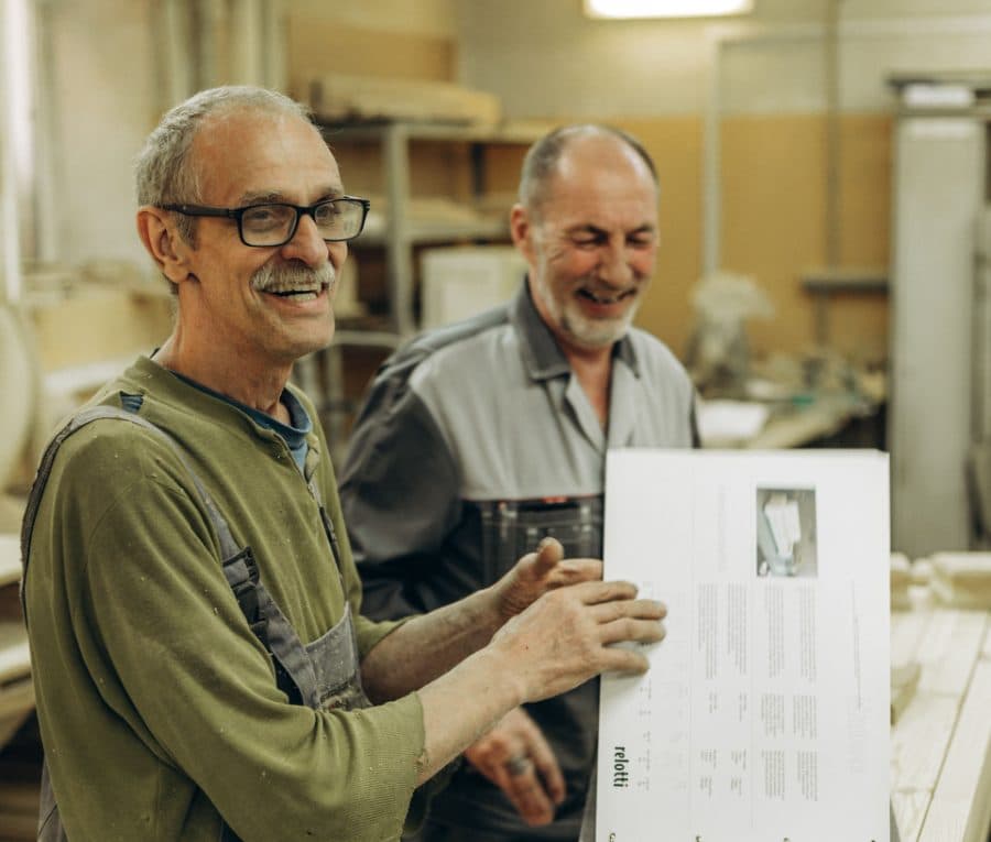 Two workshop owners laughing together over a set of plans on the factory floor